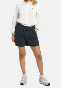 Marina atletiska shorts med elastisk midja, framfickor och en texturerad design, kombinerat med en vit skjorta med knappar.