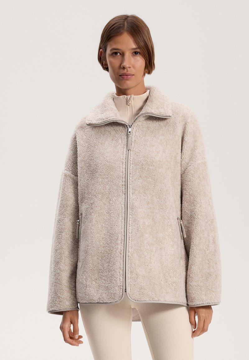 Uldent beige jakke med høj krave og lynlås foran. Har to sidelommer og en afslappet pasform. Blød tekstur og afslappet design.