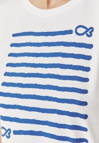 T-shirt blanc avec des motifs de coups de pinceau bleus horizontaux et un petit symbole infini bleu accentué sur le coin supérieur droit.