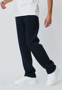 Pantalon de jogging bleu marine en tissu doux avec une coupe droite, comprenant des coutures latérales, associé à des baskets blanches.