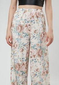 Floral-patterned wide-leg trousers in light fabric, featuring a pastel color palette with pink roses and green accents. Elastic waistband.