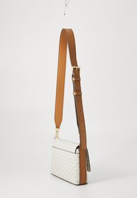 Geantă crossbody albă, cu un model, dotată cu accesorii aurii și o curea reglabilă de culoare maro, realizată din piele netedă. Formă dreptunghiulară, cu bază plată.
