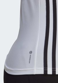 Top sportivo bianco aderente con strisce nere e logo AEROREADY. Realizzato in tessuto liscio con un design senza cuciture per garantire comfort.