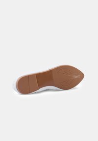 Suela de zapatilla blanca de goma con un patrón texturizado marrón, que presenta una forma alargada y puntiaguda, así como detalles elevados para mayor tracción.