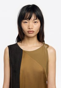 Sukienka bez rękawów z kolorowym wzorem w odcieniach czerni i dwóch odcieniach brązu. Gładki materiał z detalem w postaci wiązania na ramieniu.