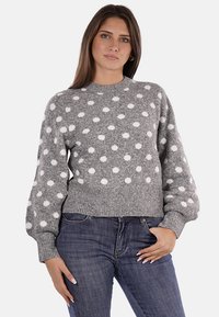 Maglione grigio con pois bianchi, polsini e orlo a costine, scollo rotondo e tessuto a maglia testurizzato. Abbinato a jeans blu.