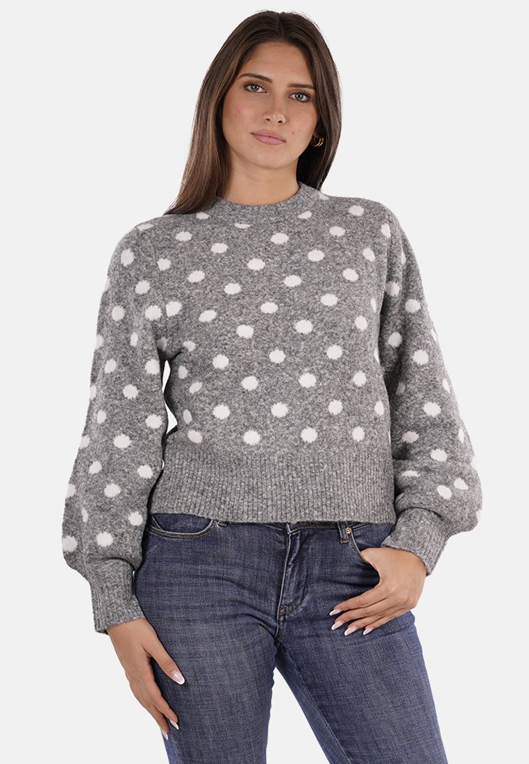 Maglione grigio con pois bianchi, polsini e orlo a costine, scollo rotondo e tessuto a maglia testurizzato. Abbinato a jeans blu.