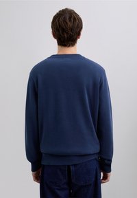 Sudadera azul marino con cuello redondo, puños y dobladillo acanalados. Textura suave, ajuste casual y diseño liso, mostrada desde atrás.