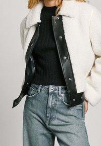 Black leather jacket with white shearling collar, paired with a black ribbed sweater and light blue denim jeans. Details include snap buttons.
