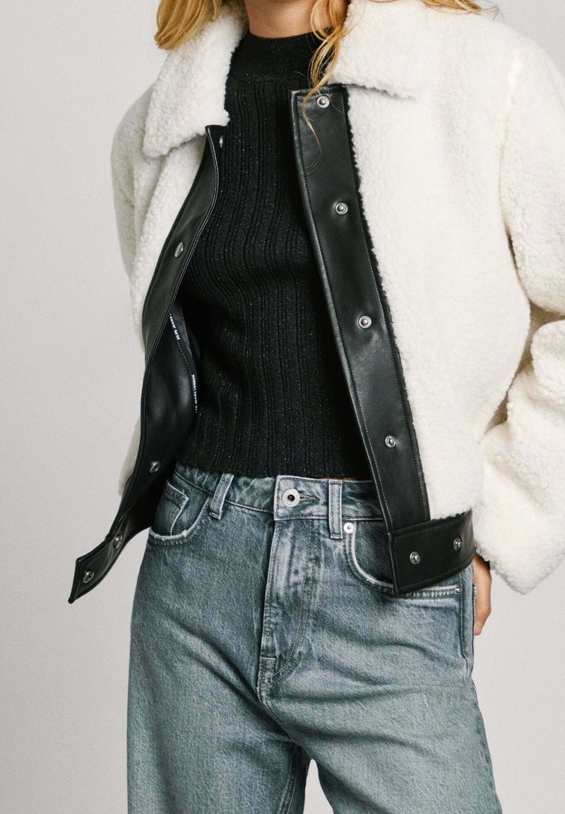 Black leather jacket with white shearling collar, paired with a black ribbed sweater and light blue denim jeans. Details include snap buttons.