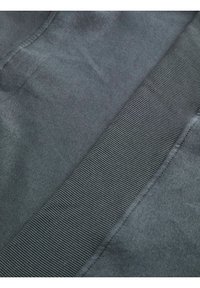 Gros plan sur un tissu gris foncé avec une bande côtelée cousue en diagonale sur la surface.