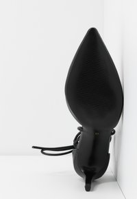 Chaussure à talon haut noire à bout pointu vue de la semelle, avec la marque de taille 37, sur un fond blanc en angle.