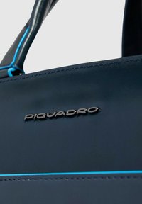 Marineblaue Ledertasche mit blauer Akzentnaht und schlankem Design; verfügt über ein metallisches Logo "PIQUADRO" auf der Vorderseite.