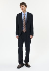 Námořnický oblek se dvěma knoflíky, upravený střih, modrá košile, hnědá pruhovaná kravata a lesklé hnědé boty. Hladká tkanina, klasický design.