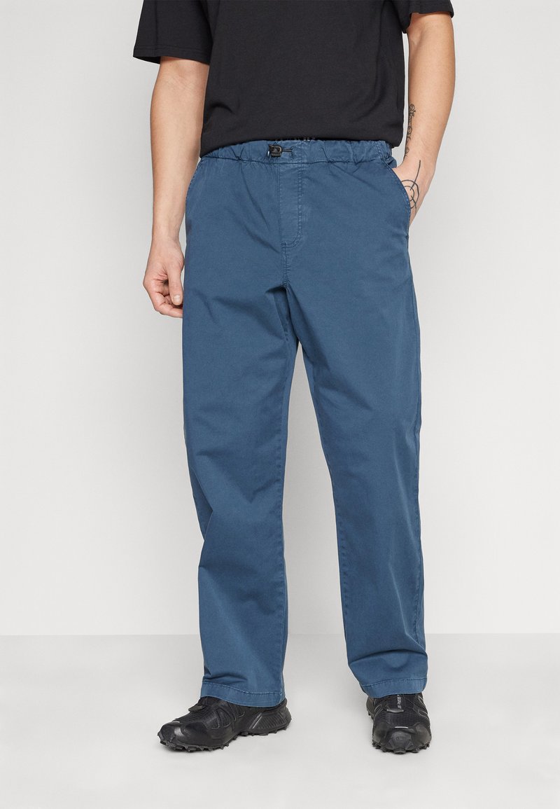 Blue cotton trousers with a relaxed fit, elastic waistband, and side pockets. Features a smooth texture and tapered leg openings.