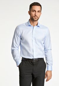 Lichtblauw langemouw shirt met een button-down kraag en subtiele textuur, gecombineerd met zwarte trainingsbroek en een zwarte riem.