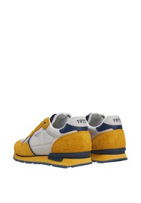 Sneakerid, millel on kollane tekstuuriga seemisnahk, valged nahast aksendid ja sinised detailid, ning kandmisel on kannal ka aastaarv "1973".