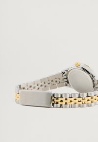 Ezüst és arany színű karóra rozsdamentes acél csattal, kerek tok, rozsdamentes acél hátlap és texturált korona részlet.