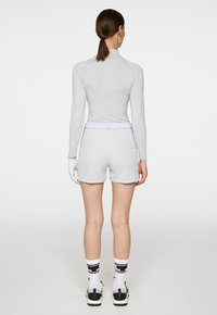 Ljusgrå långärmad tröja matchad med kortbyxor. Modellen har vita strumpor med svart mönster och svart-vita skor; handskar på handen.