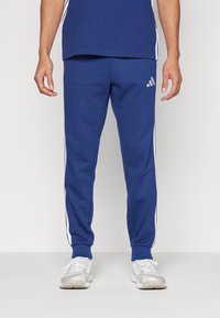 Jogging en coton bleu avec des rayures blanches sur les côtés, une coupe décontractée, des poignets côtelés et un logo brodé sur la cuisse gauche.
