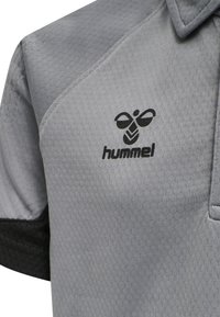 Grå sportspolo med svarta detaljer, med en texturerad tygstruktur och en svart Hummel-logotyp på bröstet. Design med kort krage.