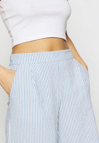 Lichtblauwe en wit gestreepte broek met een geplooid ontwerp, voorzien van zijzakken en een ontspannen pasvorm bij de taille. Gemaakt van textuurstof.