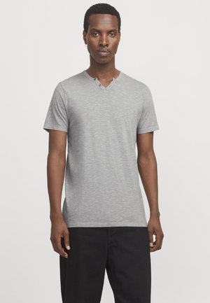 Camiseta gris de manga corta con diseño de cuello en V y una textura sutil. Presenta un detalle de botón cerca del cuello, combinada con pantalones negros.