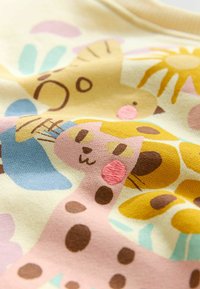 Világos sárga szövet színes állat- és virágmintákkal. Rózsaszín zsiráf, barna részletek és puha tapintású textúrák jellemzik.