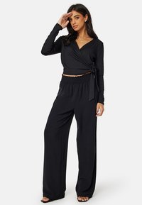 Zwarte geribbelde wikkeltop met lange mouwen en een zijstrik, gecombineerd met zwarte wijde broek met een elastische tailleband.