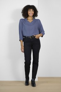 Blusa blu con scollo a V e spalle arricciate, abbinata a jeans neri aderenti e stivaletti neri alla caviglia. Tessuto semplice e liscio e silhouette classica.