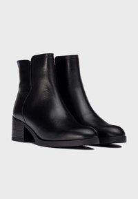 Botas de cuero negro hasta el tobillo con un acabado suave, punta semi-afilada y tacón bajo cuadrado. Presentan costuras mínimas y paneles laterales elásticos.