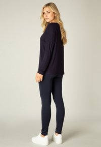 Marineblauw longsleeve shirt met een ontspannen pasvorm, gecombineerd met strakke marineblauwe leggings en witte platform sneakers, met gladde texturen en een minimalistisch ontwerp.