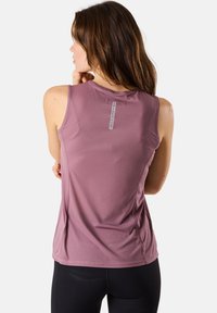 Lila ärmelloses Sportoberteil mit strukturiertem Muster, Logo auf dem Rücken und taillierter Passform, kombiniert mit schwarzen Leggings.