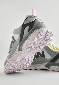 Baskets de sport grises avec des accents noirs, semelle extérieure en caoutchouc texturé et col rembourré. Présente une languette violette sur le talon.