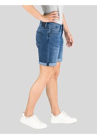 Denim shorts in een middelmatige wash, met opgerolde boorden, een medium taille en een vijf-pocket ontwerp. Ggedragen met witte sportieve sneakers.