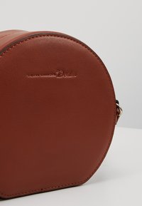 Borsa a tracolla rotonda in pelle marrone con logo del marchio impresso. Presenta metallo scorrevole e una superficie liscia, con dettagli cuciti.