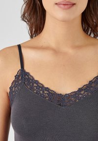 Donkergrijze camisole met een V-halslijn en intricate donkere kantafwerking. Verstelbare dunne bandjes en een nauwsluitend ontwerp. Zachte katoenstof.