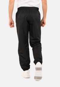 Zwarte, lichte joggingsbroek met een elastische tailleband en cuffed enkels. Bevat zijzakken en een zachte textuur. Draagt met witte sneakers.