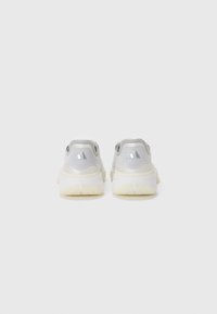 Chaussures de sport grises et blanches avec une tige texturée et des accents réfléchissants, dotées d'une semelle épaisse et rembourrée et d'un talon arrondi.