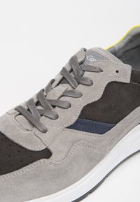 Sneaker in suede grigio con accenti grigio scuro e blu navy, caratterizzato da una tomaia testurizzata, punta rotonda e suola in gomma bianca. Cuciture dettagliate visibili.