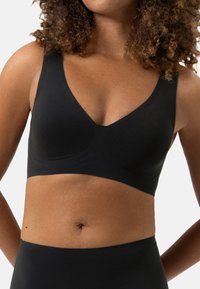 Zwarte draadloze beha met een diepe V-hals, brede bandjes, een gladde matte textuur en een naadloos cupdesign voor comfort en ondersteuning.