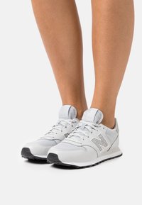 White mesh and leather sneakers featuring a textured gray accent, round toe, and flat black outsole with laces and padded tongue.