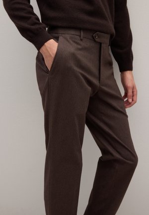 Pantalon marron texturé avec une coupe ajustée, doté de poches latérales et d'une ceinture boutonnée. Le tissu présente un motif subtil pour plus de détails.
