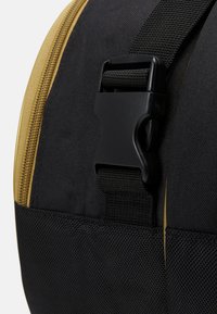 Borsa da viaggio in tessuto nero con zip dorata, dotata di una fibbia e cinghia in plastica nera, che presenta una superficie testurizzata.