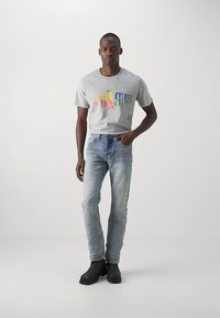 Siva majica z večbarvnim napisom, svetlo oprane jeans hlače in črni gležnjarji. Priložnostna obleka z udobnim krojem in gladko teksturo.