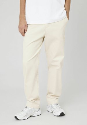 Pantalons en velours côtelé beige clair avec une coupe droite, présentant une texture côtelée subtile et des poches latérales. Associés à des baskets blanches.