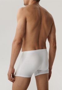 Białe bawełniane bokserki z gładkim wykończeniem, elastycznym pasem i dopasowanym krojem, przedstawione z bocznego widoku z tyłu modela męskiego.