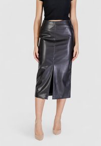 Falda midi de cuero negra con una abertura frontal, textura suave y diseño ajustado. Combinada con tacones altos en color nude.