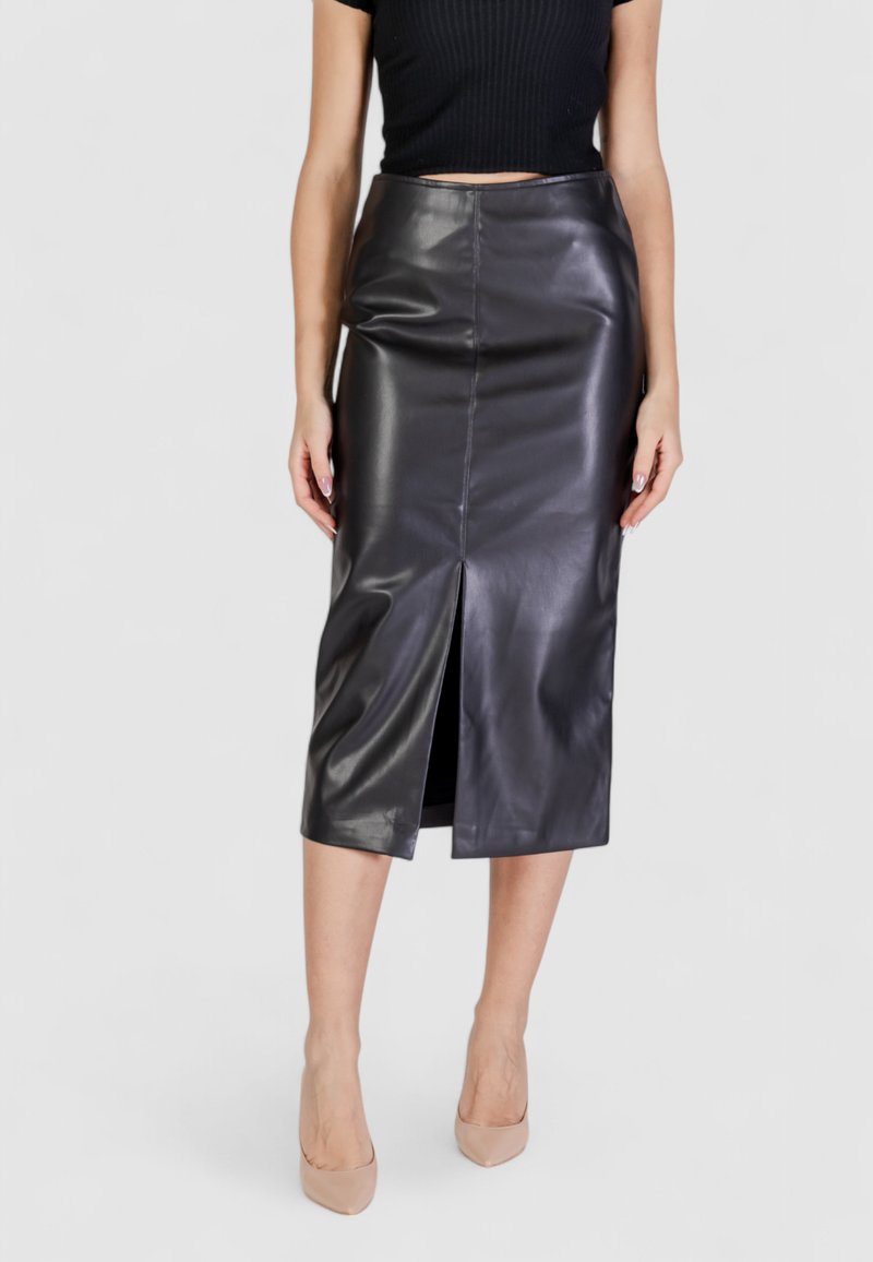 Falda midi de cuero negra con una abertura frontal, textura suave y diseño ajustado. Combinada con tacones altos en color nude.