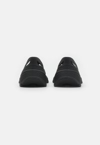 Fekete slip-on cipők barázdált textúrával, nyitott szellőzőkkel a tetején és formázott talppal. Kényelmes viseletre tervezve, minimalista profillal.